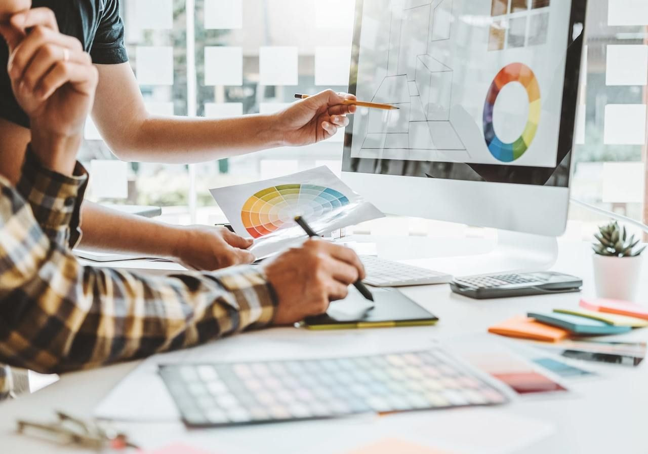 Two individuals collaborating on a computer, focused on a graphic design project displayed on the screen.